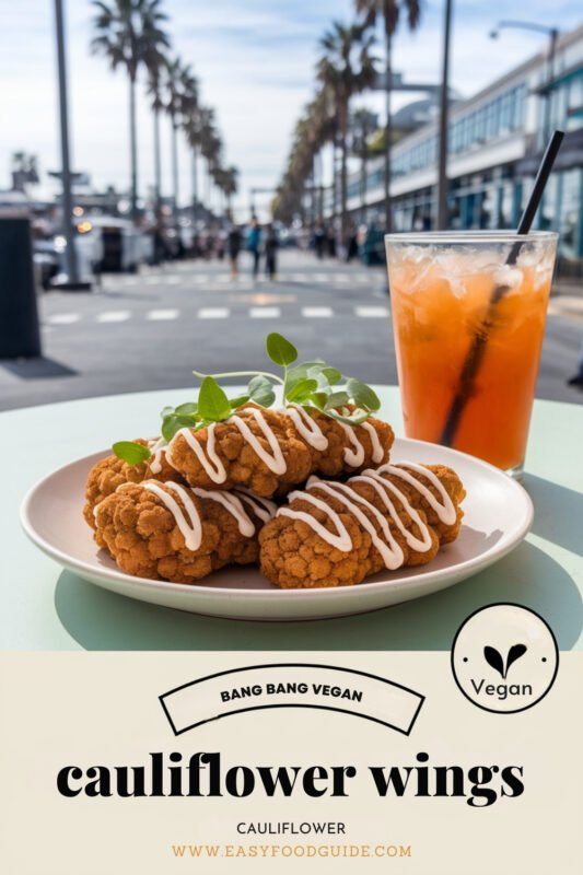 Crispy cauliflower wings drizzled with Bang Bang sauce on a rustic table with beach view.