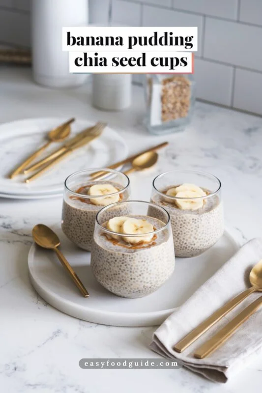 Chia seed pudding in transparent cups on marble countertop, topped with banana slices and almond butter, surrounded by gold utensils.
