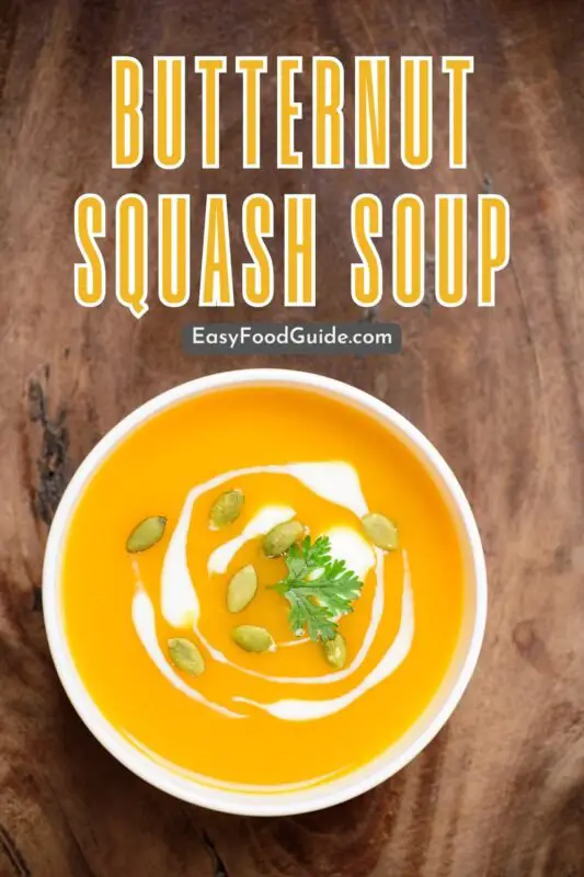 Creamy butternut squash soup in a white bowl with pumpkin seeds and dinner roll on a grey stone surface.