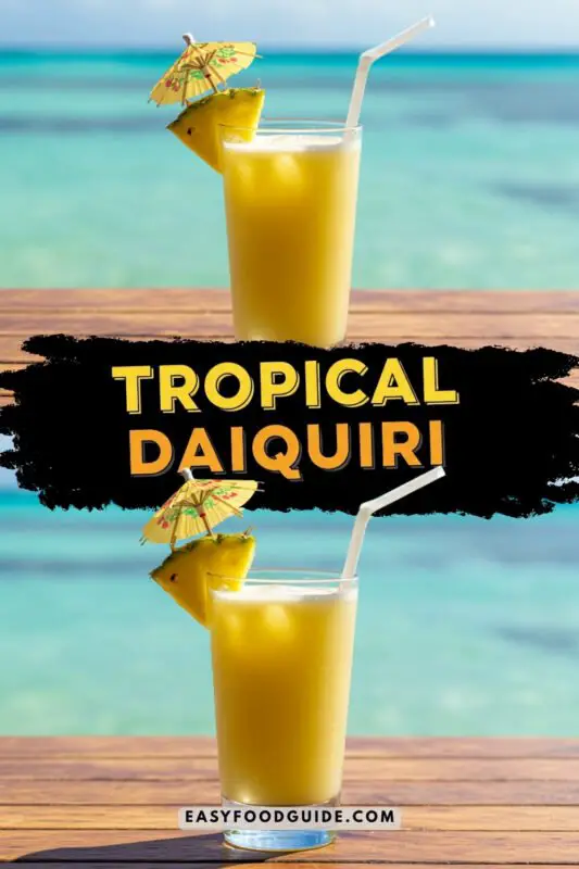 A colorful Tropical Daiquiri cocktail with pineapple and mango flavors, garnished with an umbrella, on a beach table.