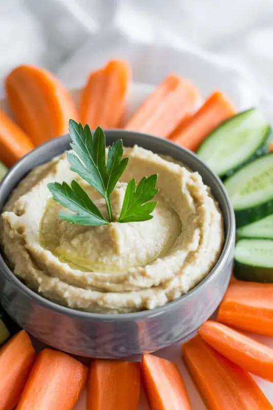 Creamy lemon garlic white bean dip in a bowl, garnished with herbs, alongside fresh vegetables and crackers.