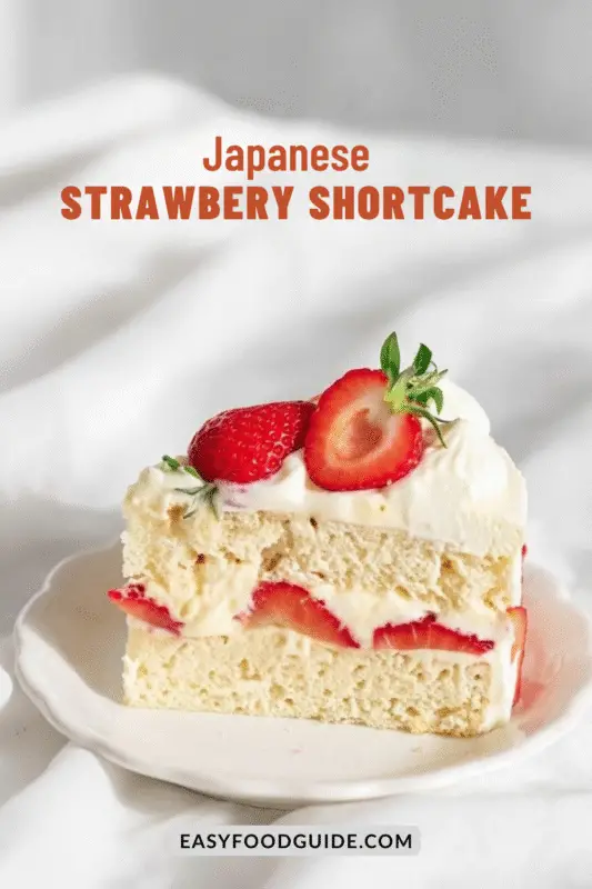 A slice of Japanese Strawberry Shortcake on a white plate, topped with strawberries and whipped cream.