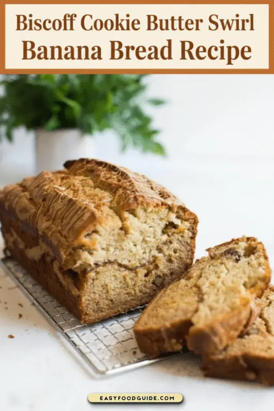 A loaf of Biscoff Cookie Butter Swirl Banana Bread on a wooden cutting board, with a slice revealing the Biscoff swirls.
