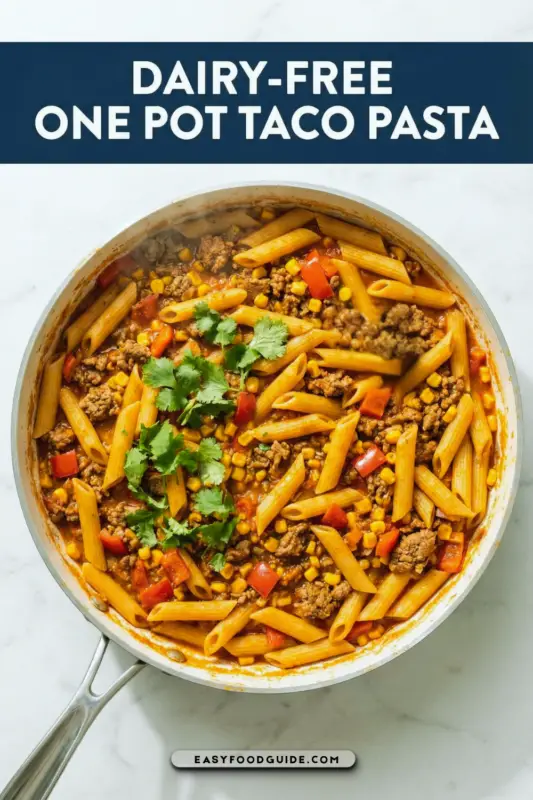 A bowl of dairy-free taco pasta with ground beef, bell peppers, and corn, garnished with cilantro, on a rustic kitchen table.