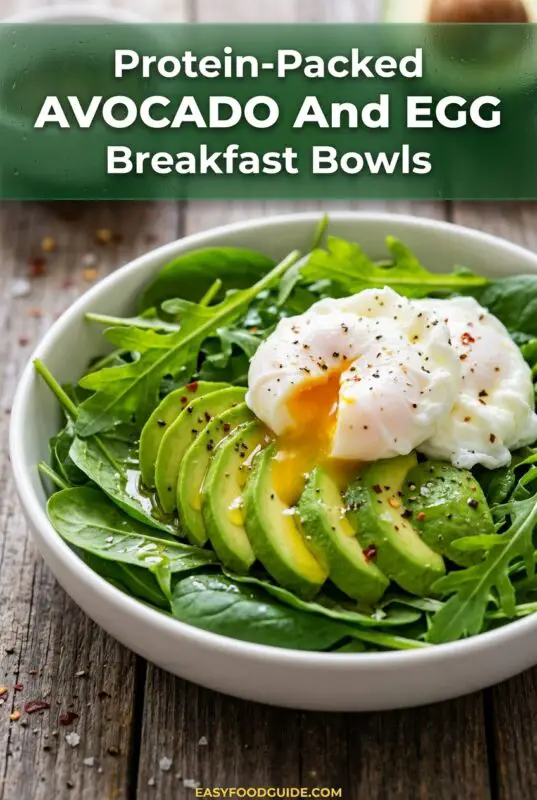 A healthy breakfast bowl with avocado, poached eggs, and greens, drizzled with olive oil on a wooden table.