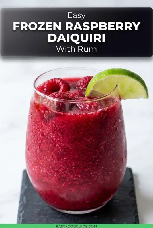 A refreshing Frozen Raspberry Daiquiri in a glass, garnished with raspberries and lime, on a sunny outdoor table.