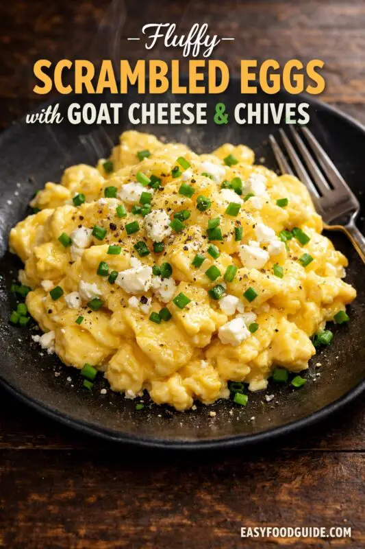 Fluffy scrambled eggs with goat cheese and chives on a rustic plate, served with toast and fresh fruit.