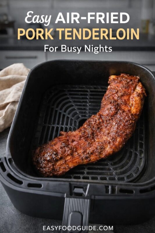 An easy air-fried pork tenderloin for busy nights, shown seasoned and cooking inside a black air fryer basket. The dish is presented in a modern kitchen setting. Text reads "Easy AIR-FRIED PORK TENDERLOIN For Busy Nights," and the website "EASYFOODGUIDE.COM" is at the bottom.