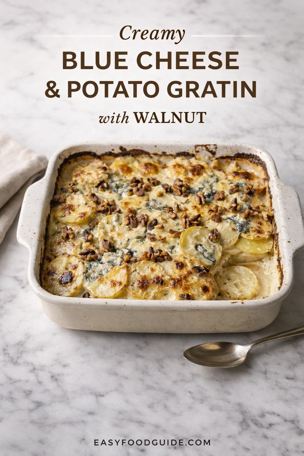 A baking dish of creamy blue cheese & potato gratin with walnut, presented on a marble countertop. The golden-brown casserole is topped with crumbled blue cheese and chopped walnuts, served with a spoon. Text reads "Creamy BLUE CHEESE & POTATO GRATIN with WALNUT," and the website "EASYFOODGUIDE.COM" is at the bottom.