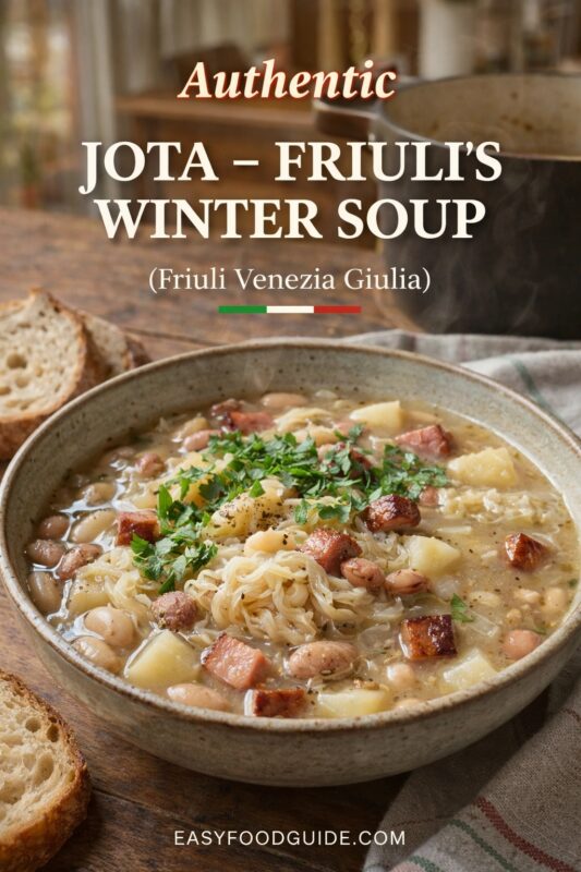 An authentic Jota – Friuli’s winter soup, presented in a rustic bowl with bread on the side. The traditional stew features beans, potatoes, and sauerkraut, garnished with parsley. Text reads "Authentic JOTA – FRIULI’S WINTER SOUP (Friuli Venezia Giulia)," and the website "EASYFOODGUIDE.COM" is at the bottom.