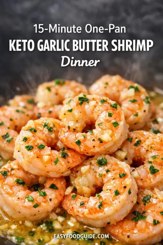 A close-up photograph of a skillet containing multiple large, cooked shrimp coated in a visible garlic butter sauce. The shrimp are pink, peeled, and generously garnished with finely chopped green parsley and minced garlic. Steam is visibly rising. Prominent text overlaid at the top reads: "15-Minute One-Pan KETO GARLIC BUTTER SHRIMP Dinner". At the bottom, a website URL: "EASYFOODGUIDE.COM".