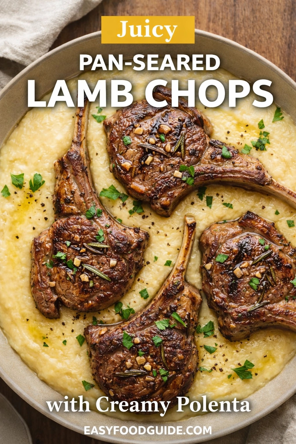 A top-down view of juicy pan-seared lamb chops served with creamy polenta in a large bowl. The seared meat is garnished with fresh herbs and garlic, creating an appetizing meal presentation. Text reads "Juicy PAN-SEARED LAMB CHOPS with Creamy Polenta," and the website "EASYFOODGUIDE.COM" is at the bottom.
