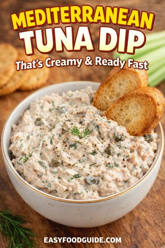 A Mediterranean tuna dip that's creamy and ready fast, served in a white bowl with toasted bread slices. The savory dip is garnished with fresh dill and capers on a wooden surface. Text reads "MEDITERRANEAN TUNA DIP That's Creamy & Ready Fast," and the website "EASYFOODGUIDE.COM" is at the bottom.
