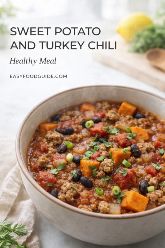 A healthy meal of sweet potato and turkey chili, served in a rustic bowl. The nutritious stew is topped with fresh herbs and green onions on a light-colored surface. Text reads "SWEET POTATO AND TURKEY CHILI Healthy Meal," and the website "EASYFOODGUIDE.COM" is visible.