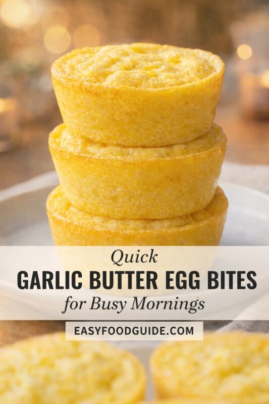 This image from EASYFOODGUIDE.COM features “Quick GARLIC BUTTER EGG BITES for Busy Mornings.” Three golden, fluffy egg bites are stacked on a white plate, with soft bokeh lights in the background. More egg bites blur softly in foreground. Text overlay highlights convenience and flavor — ideal for fast breakfasts or meal prep.