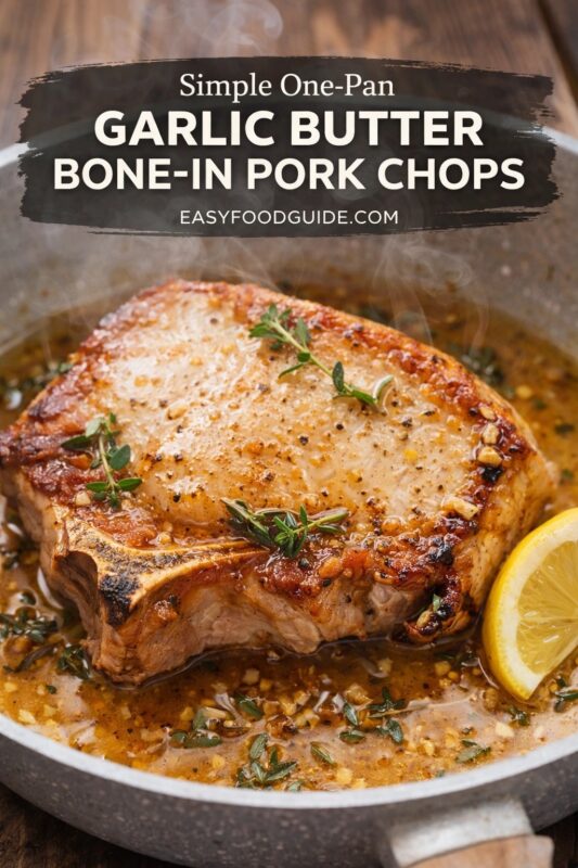 Steaming bone-in pork chop sizzles in a skillet, glazed with garlic butter sauce, minced garlic, fresh thyme, and black pepper. Lemon wedge rests beside it. Steam rises from the hot dish on rustic wood surface. Text overlay: “Simple One-Pan GARLIC BUTTER BONE-IN PORK CHOPS” + “EASYFOODGUIDE.COM” in white on dark brushstroke banner at top. Warm, savory lighting highlights texture and aroma.