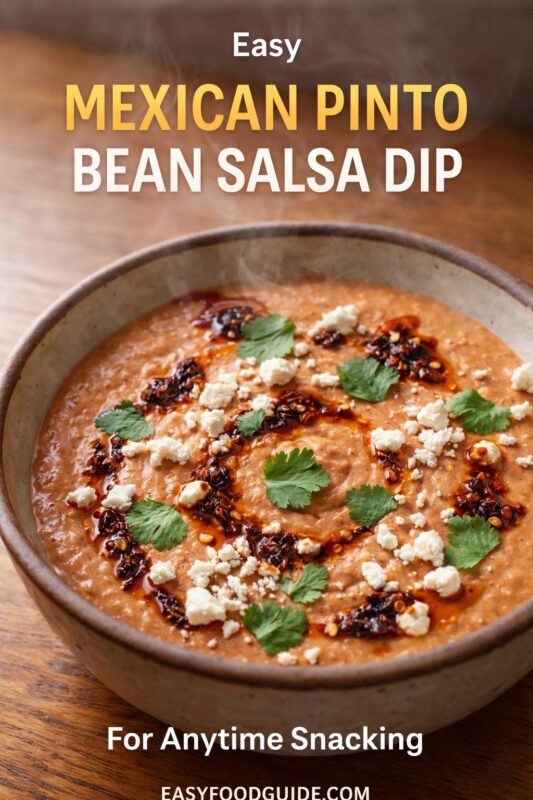 Easy Mexican pinto bean salsa dip: steaming, creamy bowl topped with crumbled cheese, fresh cilantro, and chili oil swirls. Served in rustic ceramic on wood table. Text: “Easy Mexican Pinto Bean Salsa Dip – For Anytime Snacking” + EASYFOODGUIDE.COM. Warm, inviting, versatile snack or appetizer.