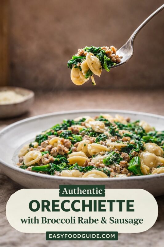 orecchiette-broccoli-rabe-sausage-3 Fork lifts steaming bite of orecchiette, broccoli rabe, and sausage above a full bowl. Dish features ear-shaped pasta, dark greens, crumbled meat, and grated cheese. Soft-focus background with small cheese bowl. Text overlay: “Authentic ORECCHIETTE with Broccoli Rabe & Sausage” + “EASYFOODGUIDE.COM” in green/cream banner at bottom. Warm, rustic lighting.