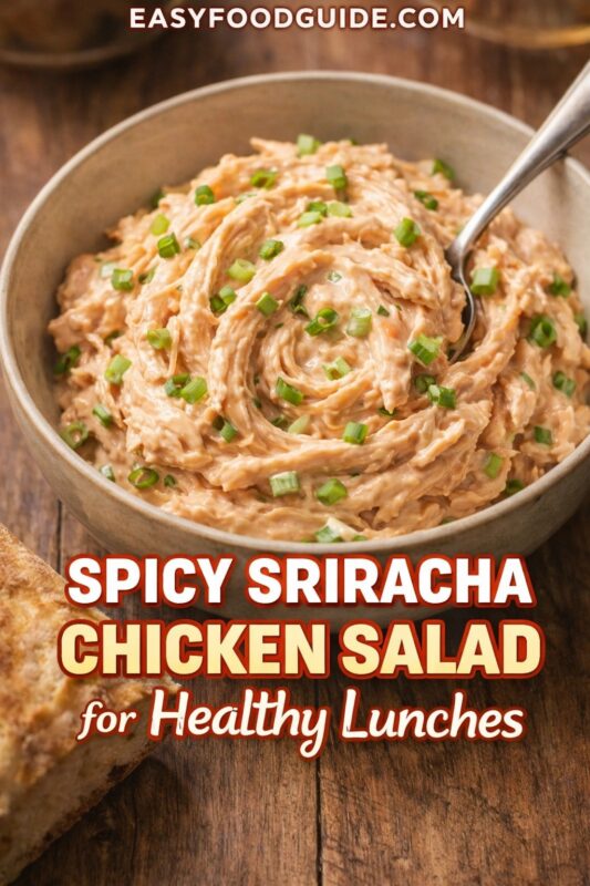 Bowl of spicy sriracha chicken salad: creamy, shredded chicken swirled with green onions, spoon resting inside. Served beside crusty bread on rustic wood table. Text: “Spicy Sriracha Chicken Salad for Healthy Lunches” + EASYFOODGUIDE.COM. Warm, inviting meal prep option.